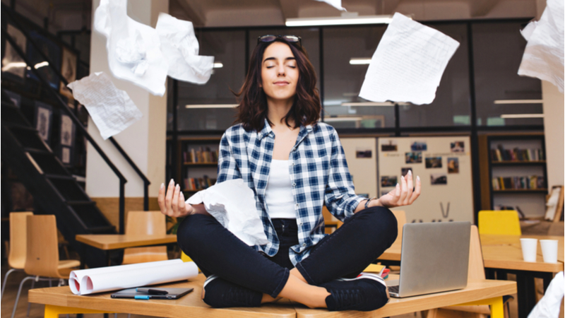 Woman meditating in office with documents flying around her