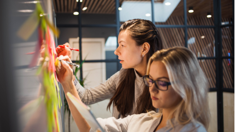 Two women writing on a whiteboard