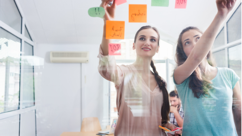 Two women pinning notes on a board