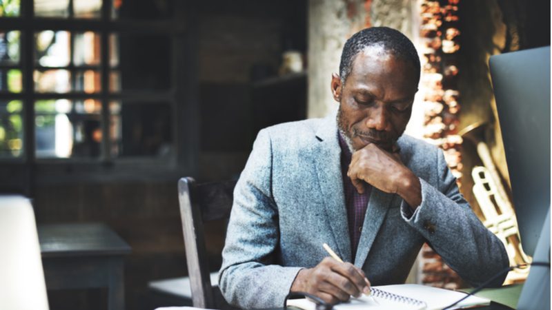 african american man in a gray suit writing in his notebook